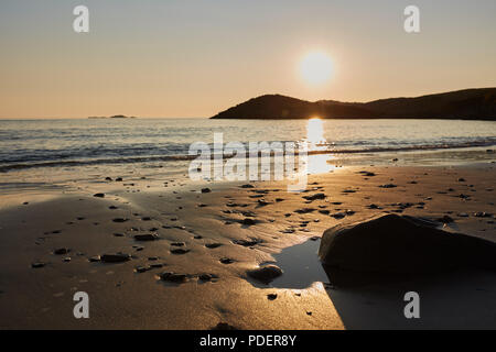 Einen goldenen sandigen Strand bei Sonnenuntergang die Sonne am Himmel und im Wasser spiegeln mit einem goldenen Glanz Stockfoto