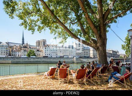 Während der Sommerveranstaltung Paris Plages gegenüber der Insel Cité und der Kathedrale Notre-Dame können die Gäste die Liegestühle eines Open-Air-Cafés an der seine genießen. Stockfoto