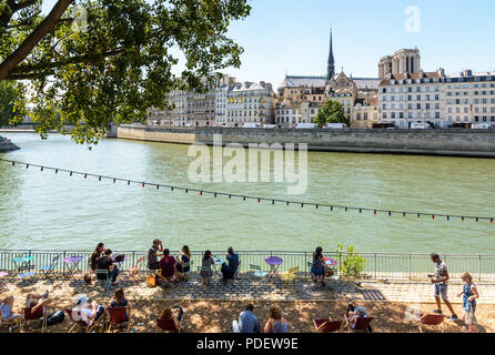 Während der Sommerveranstaltung in Paris Plages gegenüber der Insel Cité und der Kathedrale Notre-Dame genießen die Gäste die schattige Terrasse eines Open-Air-Cafés an der seine. Stockfoto
