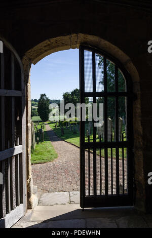 Ein Blick durch eine offene Kirche Tür in die Landschaft dahinter; die Kirche des Hl. Michael, Coxwold, North Yorkshire Stockfoto