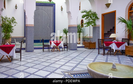 Fes, Marokko - 11. Mai 2013: marokkanische Riad Innenhof mit kunstvollen Mosaiken und maurischen Torbogen mit Tischen und Stühlen mit einem Pool eingerichtet Stockfoto