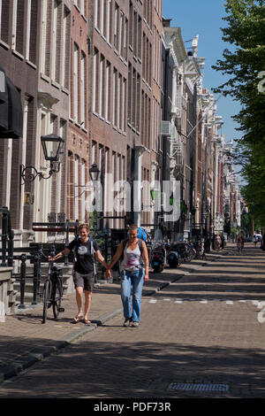 Ein schwules Paar zu Fuß in einer Straße mit typisch Holländischen Giebelhäuser Amsterdam, Holland, Niederlande Stockfoto