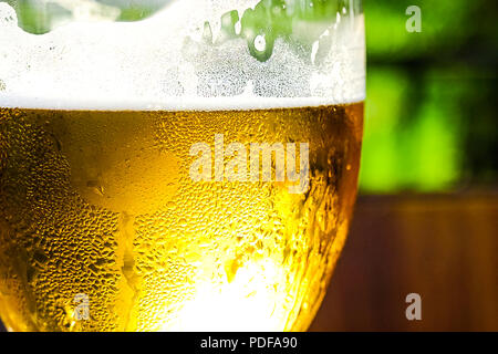 Erfrischende Apfelwein mit Eiswürfeln auf einem Holztisch. Apfelwein im Glas. Außenpool im Sommer Cafe. Vor dem Hintergrund der grünen Bäumen. Stockfoto