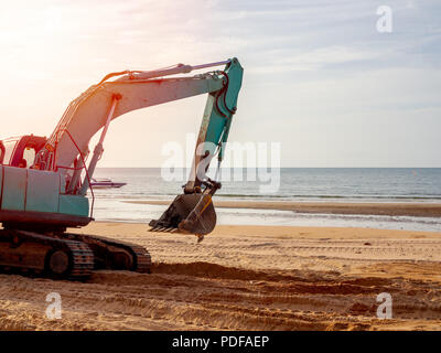 Blau oder Grün Bagger arbeiten am Strand mit Blick auf den Sonnenuntergang. Bagger Reifen Titel auf Sand mit Sonnenlicht am Abend auf marine Hintergrund Stockfoto