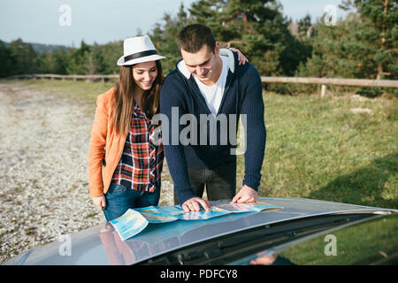 Ein junges Paar steht neben dem Auto und Suchen an der Karte die beste Route zu finden. Stockfoto
