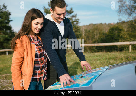 Ein junges Paar steht neben dem Auto und Suchen an der Karte die beste Route zu finden. Stockfoto