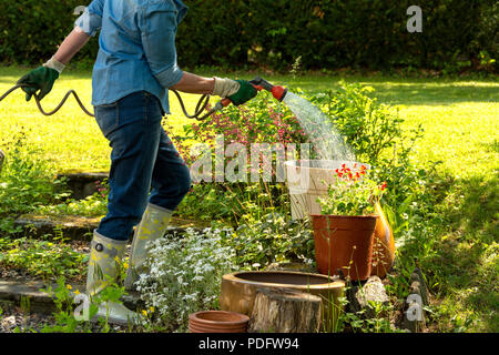 Frau Bewässerung ihrer Blumen in seinem Garten Stockfoto