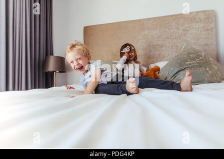 Happy Kids spielen im Schlafzimmer. Kleiner Junge lächelnd mit Mädchen an der Rückseite in der Krone auf dem Bett. Stockfoto