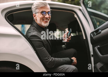 Portrait von lächelnden reife Geschäftsmann auf dem Rücksitz eines Cab sitzen. Mann, ein Taxi zu nehmen, für das Reisen. Stockfoto