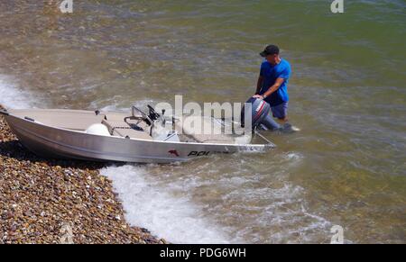 Mann mit einem teilweise überfluteten Strände Aluminium Boot. Sidmouth Strand. East Devon, Großbritannien. August, 2018. Stockfoto