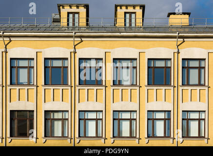 Die Fassade des alten Gebäudes mit gelben Wänden und weißen Dekor an den Fenstern. Oberen Etagen, Dach und Himmel Stockfoto