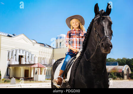 Blonde Jugendmädchen reiten Sanftes schwarzes Pferd Stockfoto