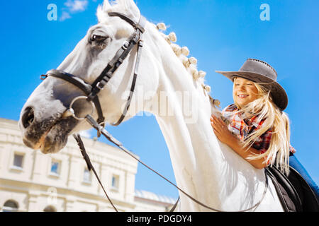 Lächelnd cute Cowboy girl stützte sich auf ihre weißen Racing Pferd Stockfoto