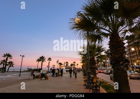 LARNACA, ZYPERN - Januar 5, 2018: Die Menschen auf dem Bürgersteig an Finikoudes Strand, einem Spaziergang bei Sonnenuntergang. LARNACA, 5. Januar 2018 Stockfoto