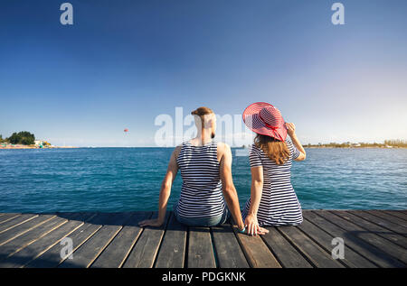 Romantisches Paar in gestreiften Kleid sitzt auf Pier und Suchen im Blue Lake Issyk Kul in Kirgisistan. Sommer und Meer Konzept. Stockfoto