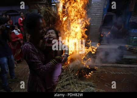 Bhaktapur, Nepal. 9 Aug, 2018. Ein Kind reagiert, nachdem ihre Mutter sie um ein Feuer und Rauch, wo ein Stroh Bildnis des mythischen Daemon' Ghanta Karna' während der Feierlichkeiten der Hindu festival Gathemangal in Bhaktapur verbrannt wurde, am Stadtrand von Kathmandu, Nepal, 01. August 2016 schaukeln. Einheimische Bhaktapur für das Festival versammelt, in dem Glauben, dass brennendes Stroh Bildnisse des Daemon wehrt Krankheiten von Kindern. Credit: Skanda Gautam/ZUMA Draht/Alamy leben Nachrichten Stockfoto