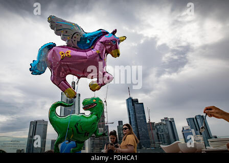 Frankfurt am Main, Deutschland. 09 Aug, 2018. Zwei Gasgefüllte Luftballons in Form eines Dinosauriers (unten) und ein Einhorn sind durch eine Folge von zwei Kindern auf der Terrasse eines Cafés in der Innenstadt vor dem Hintergrund der Skyline der Stadt statt. Foto: Frank Rumpenhorst/dpa/Alamy leben Nachrichten Stockfoto