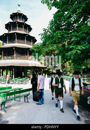 München, Deutschland - 29. Juli 2018: Traditionell gekleidete Bayerischen Männer neben dem Chinesischen Turm im Englischen Garten. Muslimische Frau in voller schwarzen Schleier Stockfoto