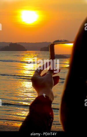 Hand der Frau verwenden smart phone Foto der Sonnenuntergang am Ao Nang Beach, Krabi, Thailand. Stockfoto