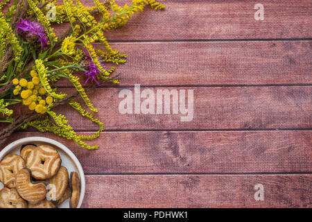 Herbst gemütliche Zusammensetzung von Blumen und Cookies auf dunklem Hintergrund. Herbst Konzept. Flache Layout, Ansicht von oben Stockfoto