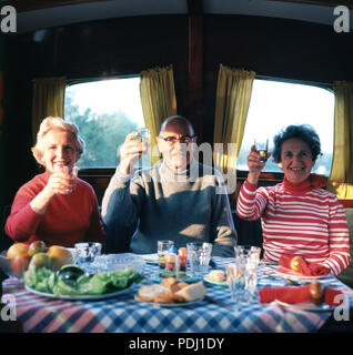 1960 s, Prost, auf dem Wasser auf den Norfolk Broads, drei Leute heben ihre Gläser vor einer Mahlzeit Ihren Bootsurlaub, Norfolk, England, UK zu feiern. Stockfoto