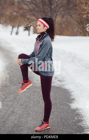 Portrait der Kaukasischen jungen Frau, dehnen und Aufwärmen für Joggen im Winter Park. Mädchen trainieren im Freien Sportkleidung tragen, Kopfbügel Stockfoto