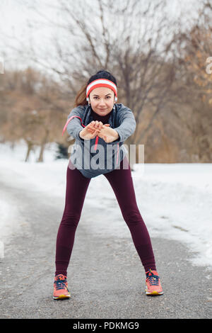 Portrait der Kaukasischen jungen Frau, dehnen und Aufwärmen für Joggen im Winter Park. Mädchen trainieren im Freien Sportkleidung tragen, Kopfbügel Stockfoto