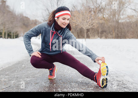 Portrait der Kaukasischen jungen Frau, dehnen und Aufwärmen für Joggen im Winter Park. Mädchen trainieren im Freien Sportkleidung tragen, Kopfbügel Stockfoto