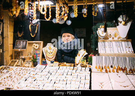 Riga, Lettland - 18 Dezember, 2017: Junge Frau Verkäufer verkauft verschiedene Schmuck aus Bernstein. Traditionelle Souvenirs am europäischen Markt. Souvenir aus Balt Stockfoto