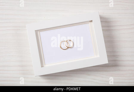 Liebe und Ehe Konzept. Goldene Hochzeit Ringe auf einem leeren weißen Bilderrahmen, Ansicht von oben, auf einem weißen Hintergrund Holz isoliert. Stockfoto