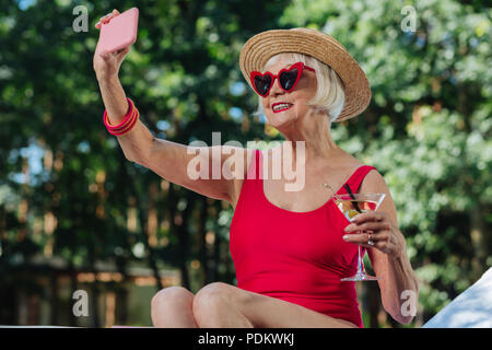 Strahlende blonde reife Frau, die Foto mit Martini Stockfoto