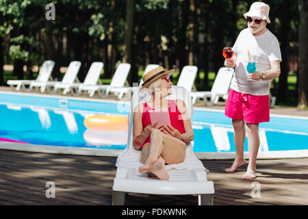 Pensionierter Mann, der rote Shorts, Cocktails, seine Frau Stockfoto