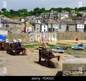 Die Leute sitzen auf einer Bank im Mousehole Harbour, Cornwall, England, Großbritannien Stockfoto