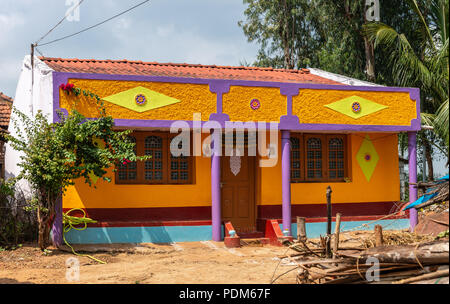 Nilavagilukaval, Karnataka, Indien - November 1, 2013: Leuchtend orange, gelb und lila lackiert neu gebaute Haus steht im braunen Schmutz unter Licht bl Stockfoto