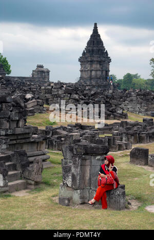 Dame in Rot setzte sich auf einige Steine, Prambanan Tempel, Yogyakarta, Java, Indonesien. Stockfoto
