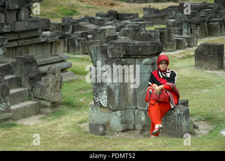 Dame in Rot setzte sich auf einige Steine, Prambanan Tempel, Yogyakarta, Java, Indonesien. Stockfoto