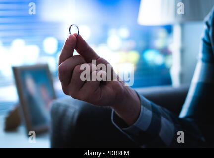 Mann, Verlobung oder Hochzeit Ring in der Hand über Vorschlag oder Scheidung denken in der Nacht spät nach Hause. Beziehung oder Eheprobleme. Stockfoto