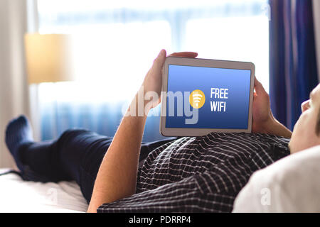 Mann mit der kostenlosen Hotel Wifi mit Tablet. Liegen im Hotel Zimmer Bett und im Internet surfen. Zugang der Öffentlichkeit online und Anschluss für Kunden zur Verfügung. Stockfoto