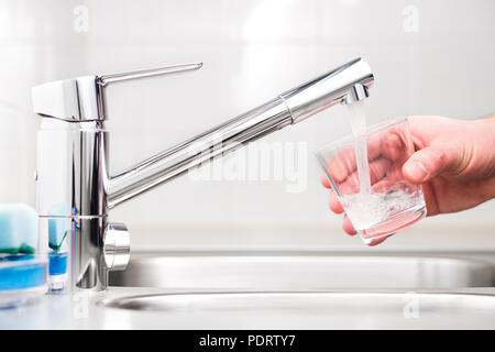 Füllung Glas mit Leitungswasser. Moderne Hahn und Waschbecken in der Küche zu Hause. Man gießt Frisches trinken bis in die Tasse. Stockfoto