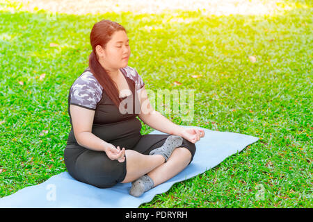 Asiatische Fett plus größe Mädchen sitzen Yoga auf der Matte im grünen Garten Park Stockfoto