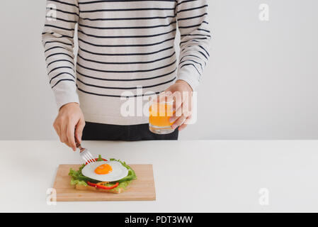 Die Hände des Menschen schneiden Sie die Eier auf Papier, serviert mit Brot, Kräutern, Wurst und frischem Saft. Stockfoto
