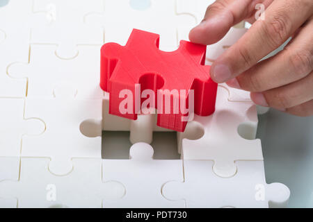 Nahaufnahme der Hand ein Geschäftsmann Anschluss rot Stück in Weiß Jigsaw Puzzles Stockfoto