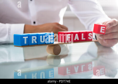 Der Geschäftsmann hand Balancing true und false Blöcke auf Holz- Wippe über Schreibtisch Stockfoto
