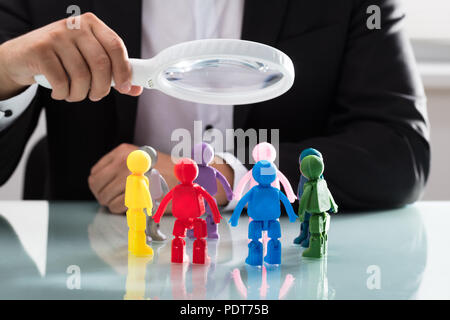 Der Unternehmer Hand mit Lupe über mehrfarbige menschliche Figuren auf reflektierenden Schreibtisch Stockfoto