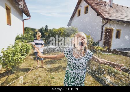 Kinder Spaß mit Spritzwasser. Geschwister auf dem Hinterhof des Hauses im Sommer Tag. Stockfoto