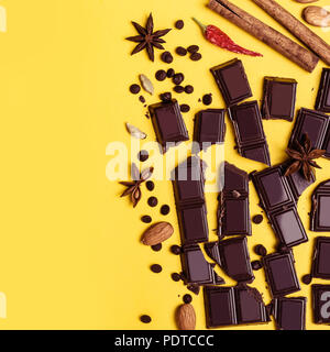 Stücke Schokolade, Zimt, Gewürze und Mandeln auf einem gelben Hintergrund. Stockfoto