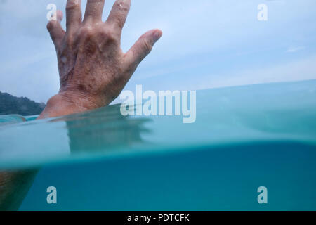 Hälfte ist eine 50 Jahre alte Frau unter Wasser im Meer und die Finger über dem Wasser hinter ist blauer Himmel und grünen Bäumen, Stockfoto