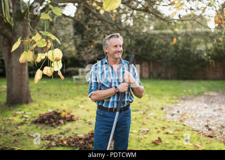 Lächelnd älterer Mann harken Blätter im Herbst im Hinterhof Stockfoto