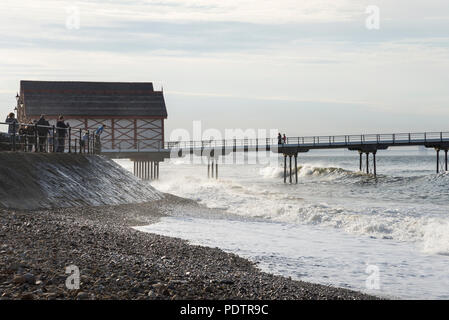 Leute, die Wellen am Strand brechen in Saltburn-by-the-Sea, North Yorkshire, England. Stockfoto