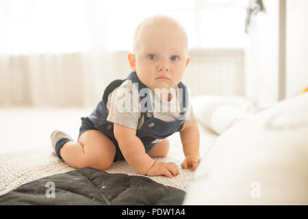 Traurig kleinkind Strampler und t-shirt kriecht auf dem Teppich im Zimmer gegen die Fenster. Stockfoto